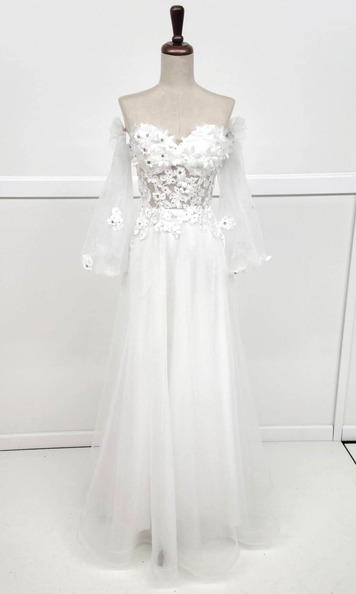 The Chicas CHF3096 Long Sleeve Long Prom Ball Gown features an off-shoulder design, sheer long sleeves, floral lace appliqué bodice, and a flowing tulle skirt—ideal for anyone seeking an elegant evening or romantic ball gown style.